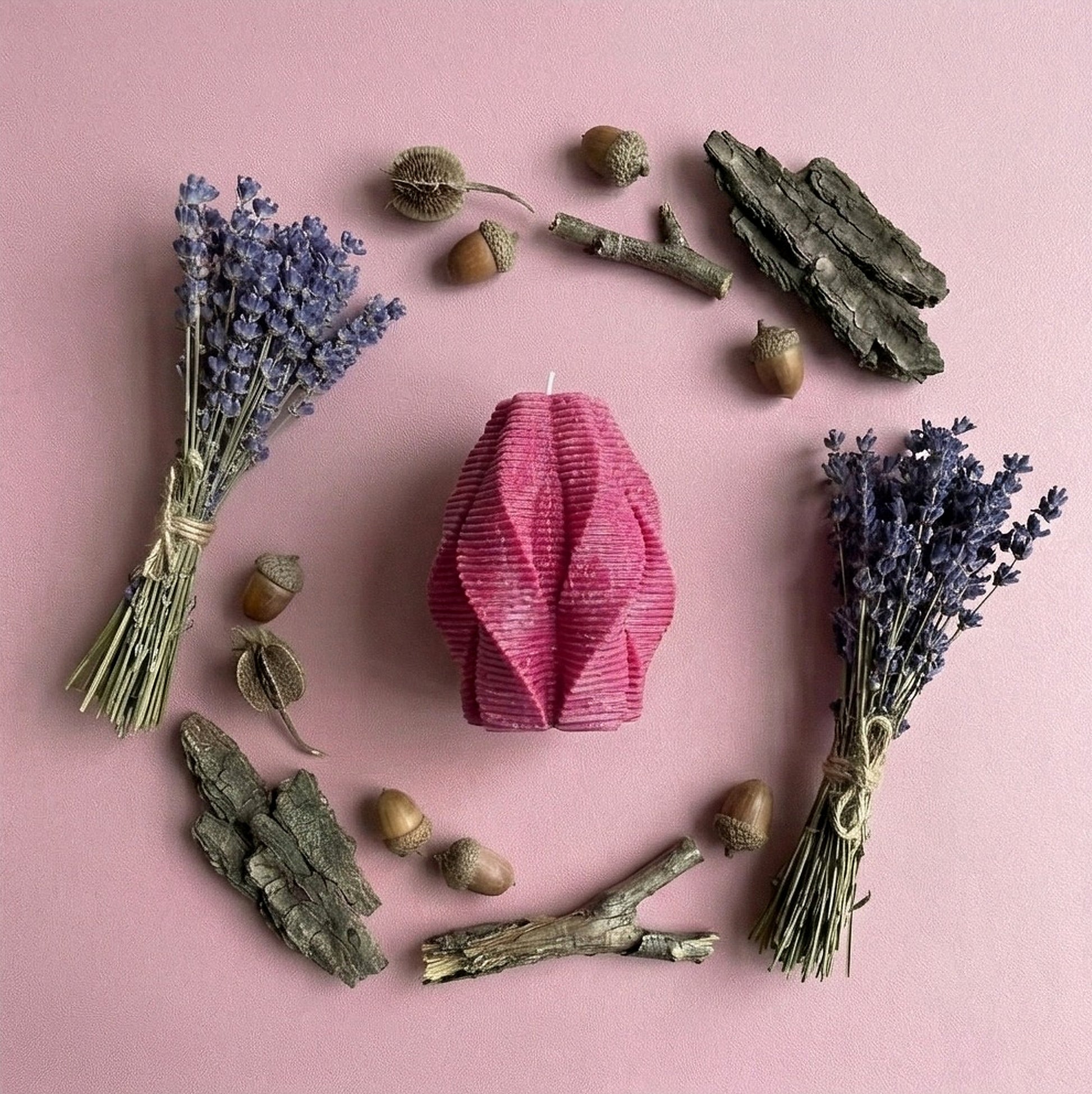 Pink candle surrounded by lavender, acorns, and branches on a pink background