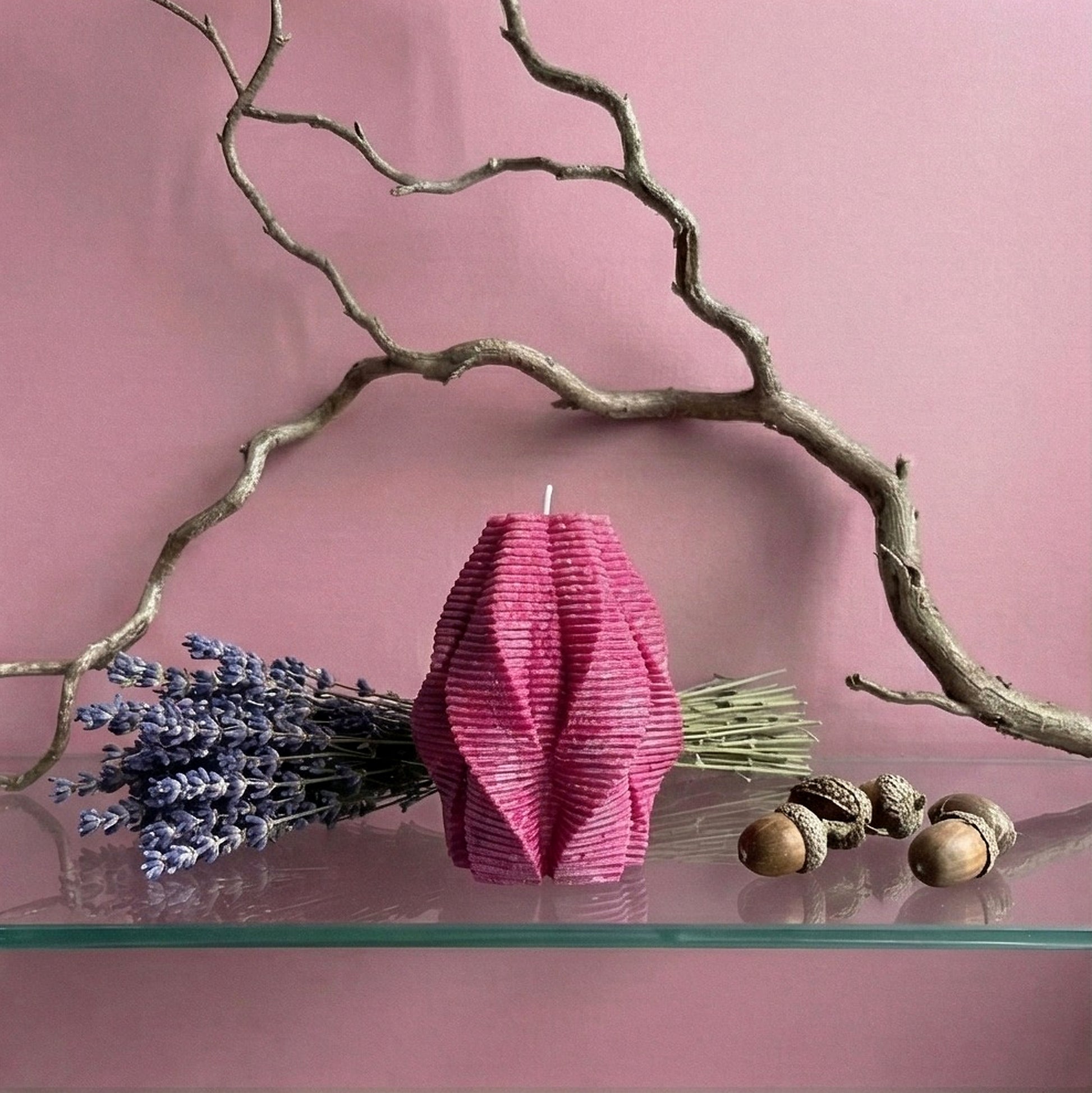 Pink textured candle with lavender, acorns, and branches on a pink background
