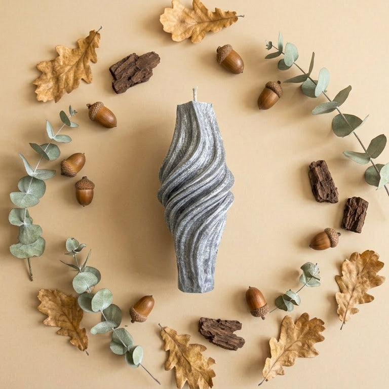 Textured candle surrounded by eucalyptus leaves and acorns on a beige background