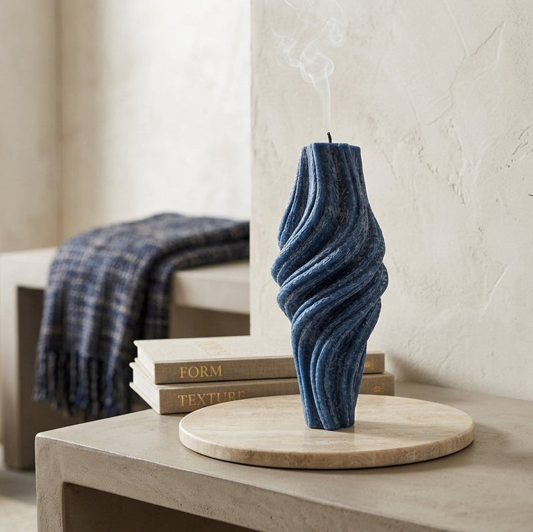 Blue candle on a wooden stand with a vase of dried flowers in a room setting.