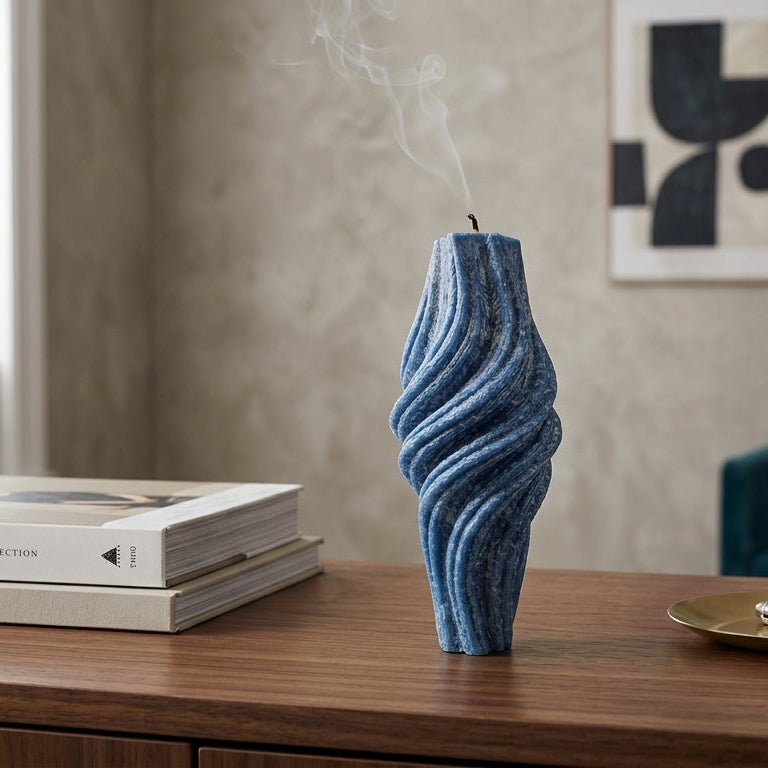 Blue textured candle on a wooden surface with books and a pen in the background