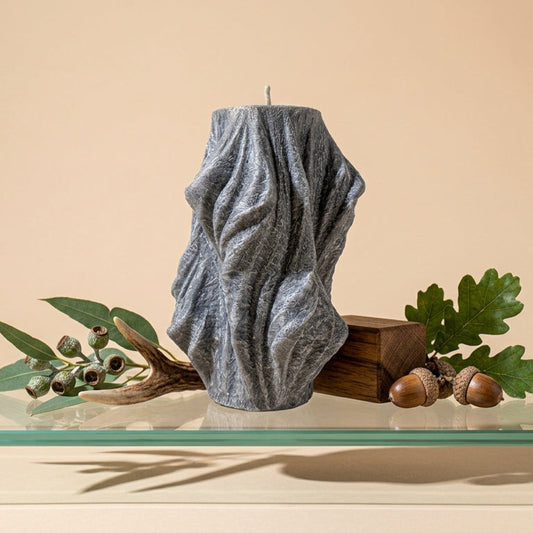 Textured gray candle on a glass surface with greenery and acorns