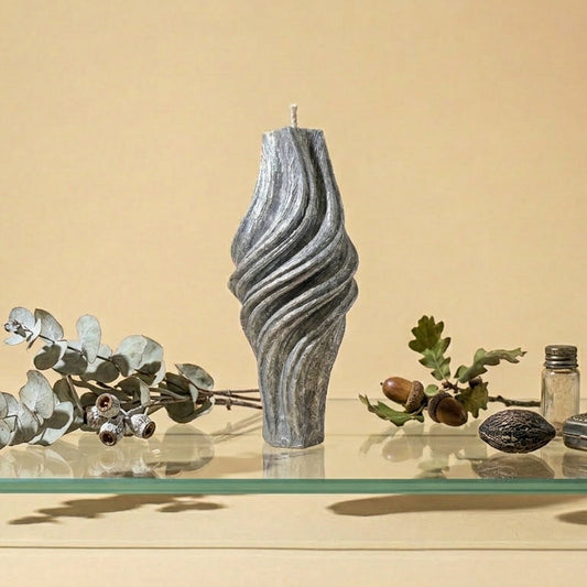 Decorative candle with wavy texture on a glass surface with flowers and small objects.