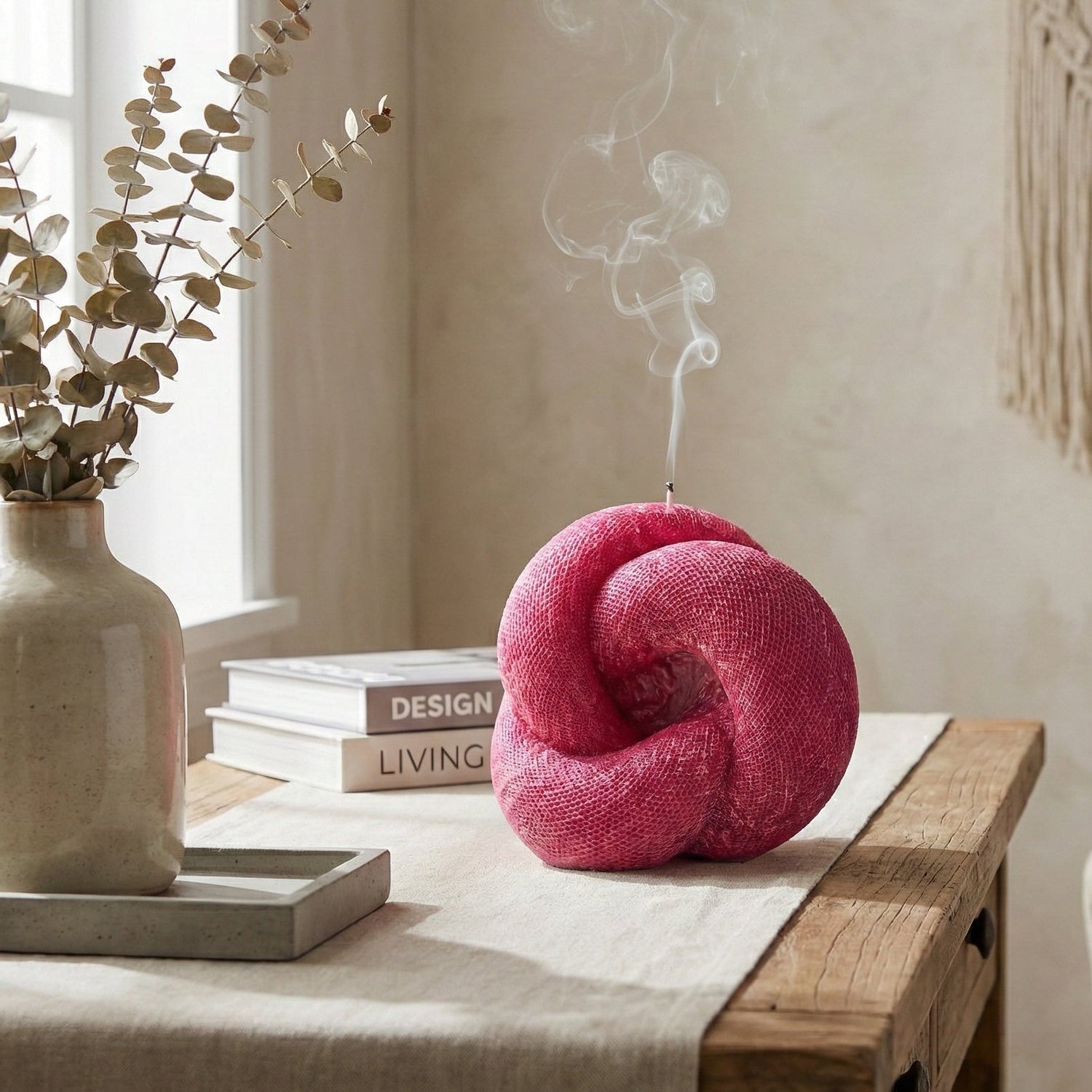 Pink knitted ball incense burner on a wooden table with books and a vase in a room setting.
