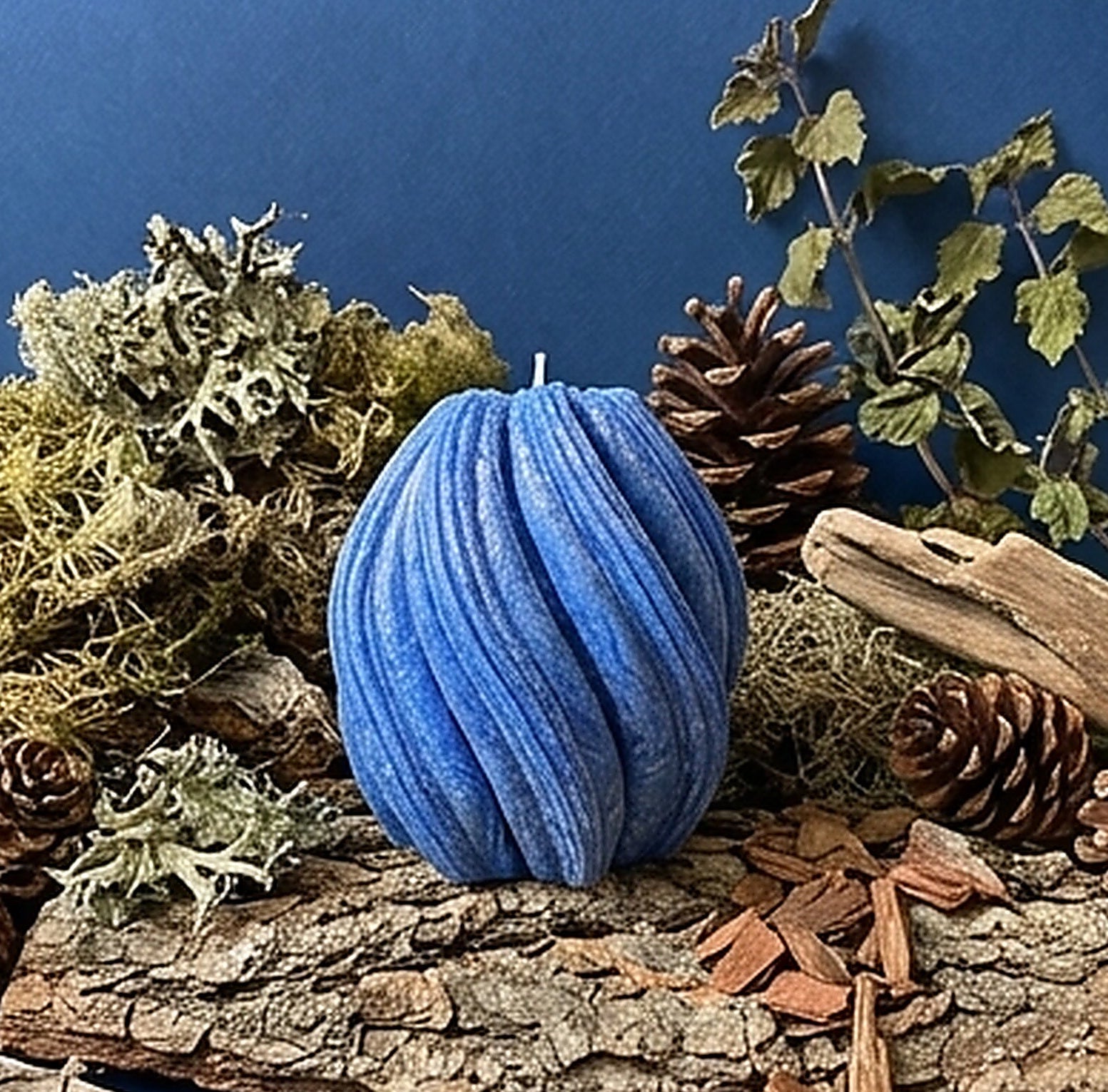 Blue candle surrounded by natural elements like wood, pinecones, and moss on a blue background