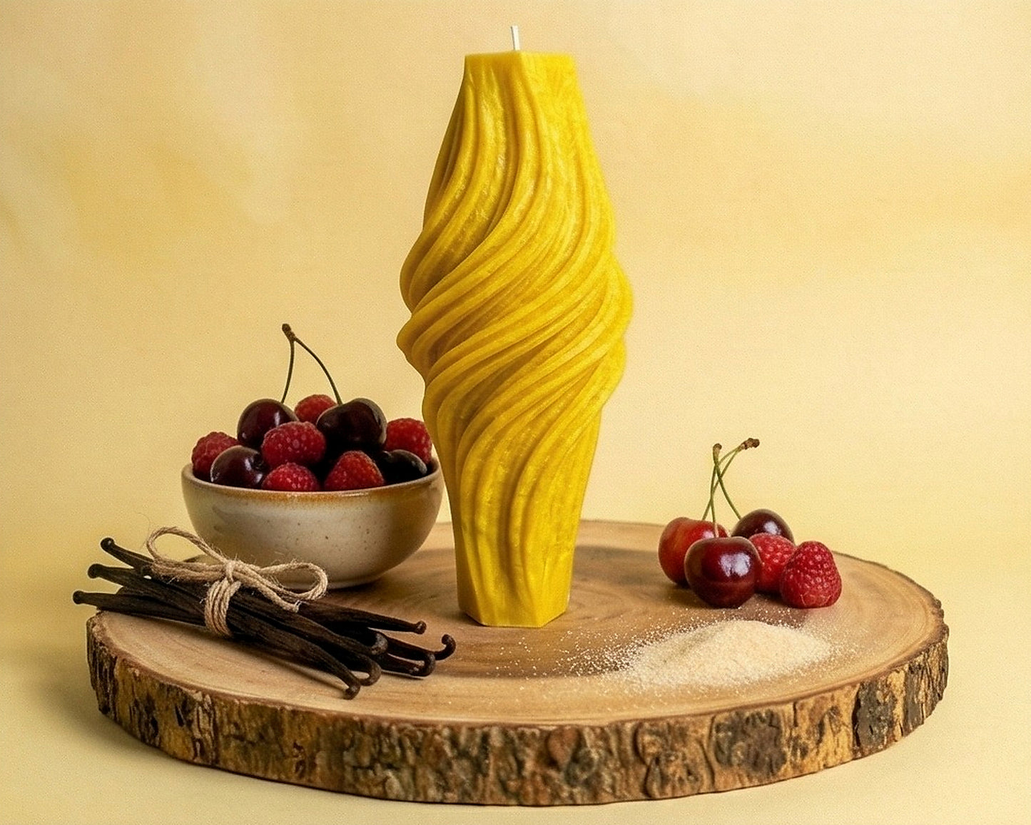 Yellow textured candle on a wooden platform with berries and vanilla beans.