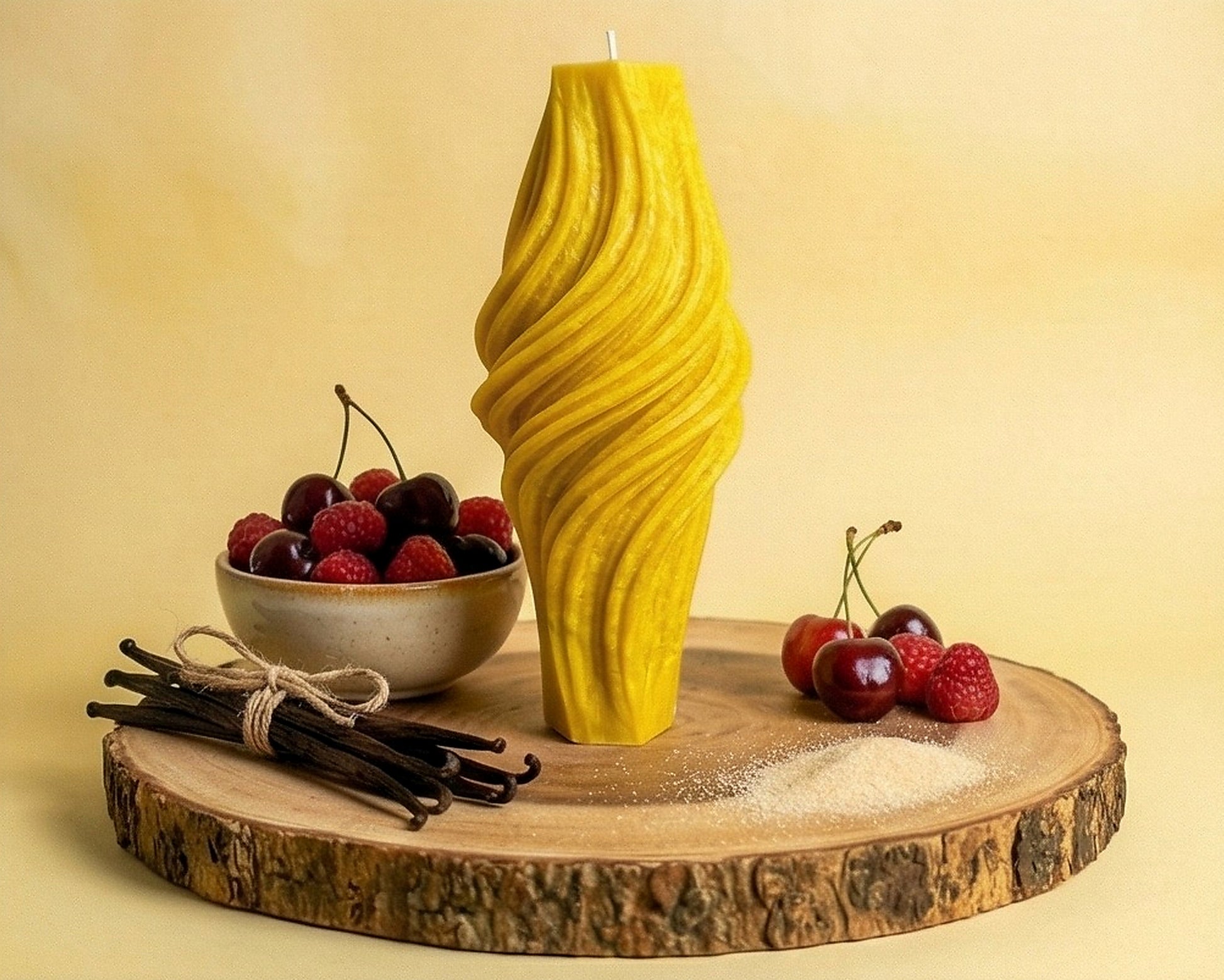 Yellow textured candle on a wooden platform with berries and vanilla beans.