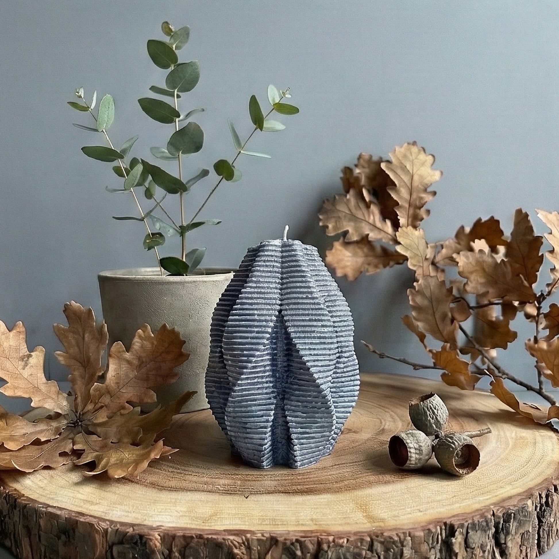 Decorative candle on a wooden surface with leaves and a plant in the background