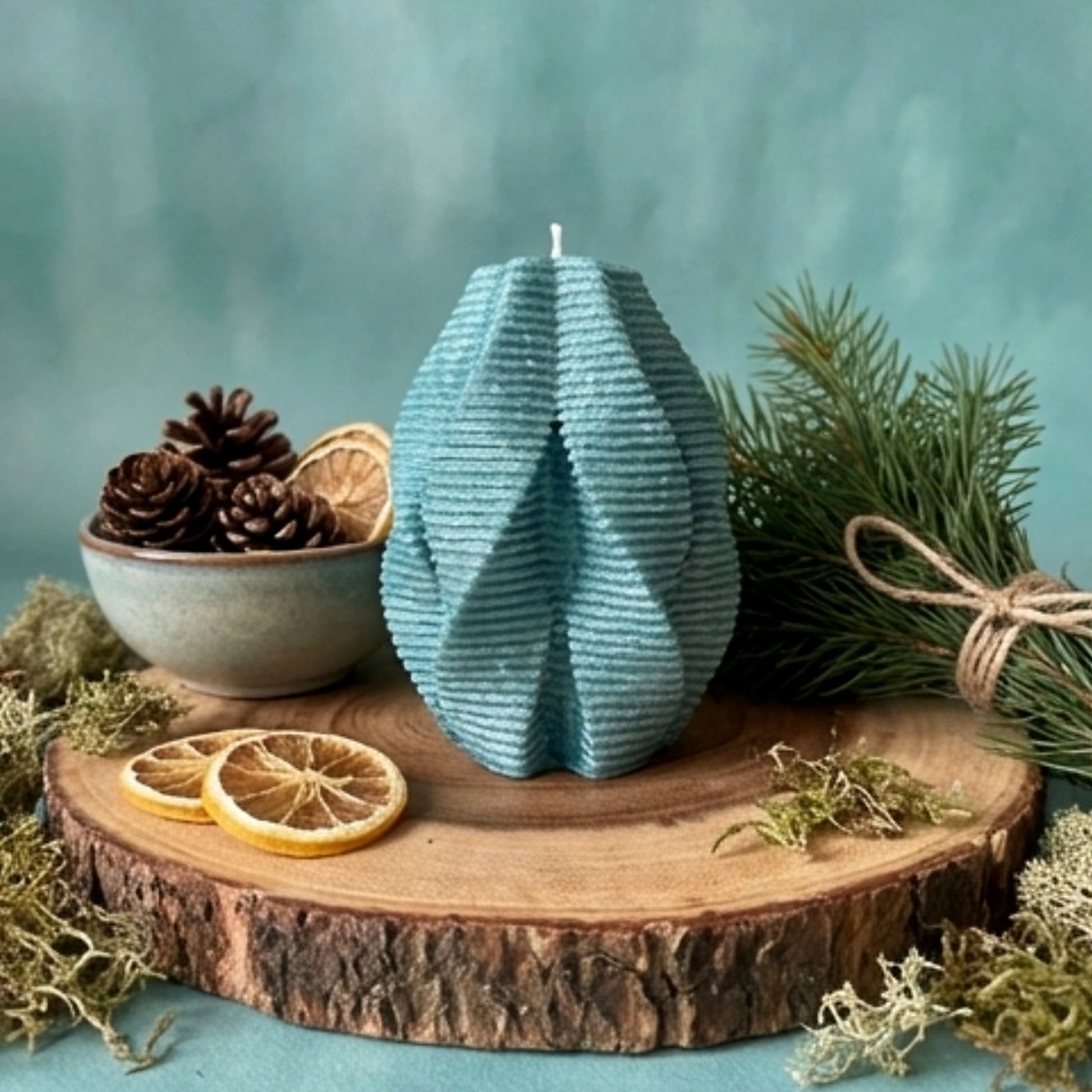 Blue textured candle on a wooden stand with decorative elements on a teal background